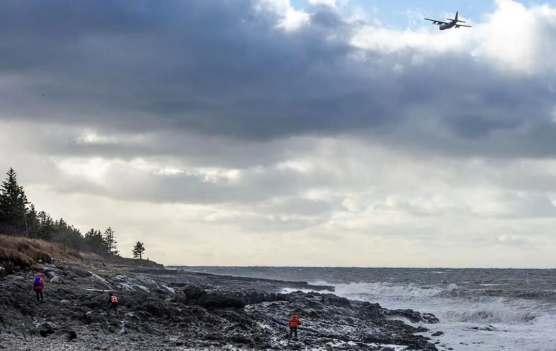 An RCAF Hercules aircraft scours the waters as members of a ground search and rescue team walk along the shore of the Bay of Fundy in Hillsburn, N.S., in an area where empty life-rafts from a scallop fishing vessel were reported on Dec. 15, 2020. (Andrew Vaughan/The Canadian Press)