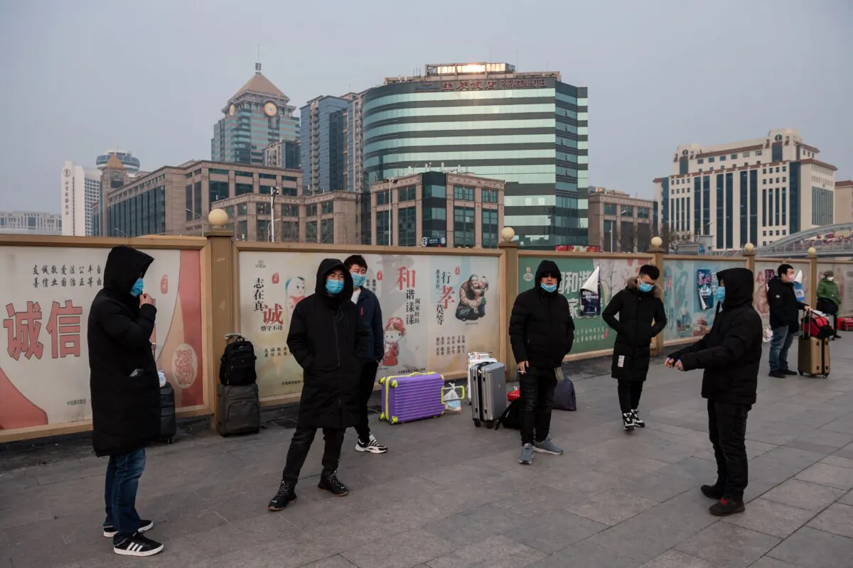 People wearing masks wait next to their suitcases at the Beijing railway station in Beijing on Jan. 27, 2020. (Nicolas Asfouri/AFP via Getty Images)