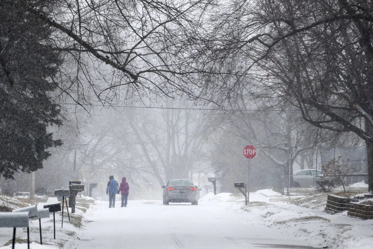 Two people hold hands while walking south on Madison Street toward 27th Avenue in Bellevue, during a winter storm warning, Neb., on Jan. 25, 2021. (Chris Machian/Omaha World-Herald via AP)