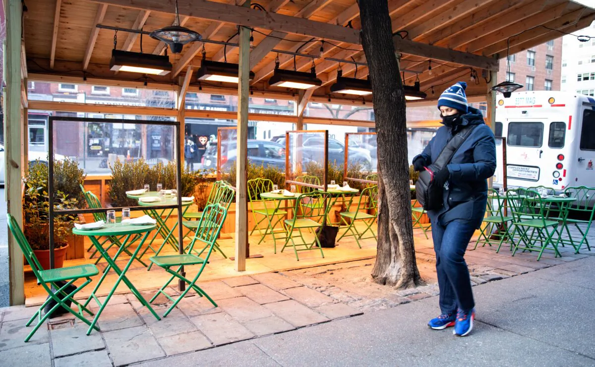 A woman wearing a mask during the CCP virus pandemic walks past an empty restaurant in New York on Jan. 20, 2021. (Chung I Ho/The Epoch Times)