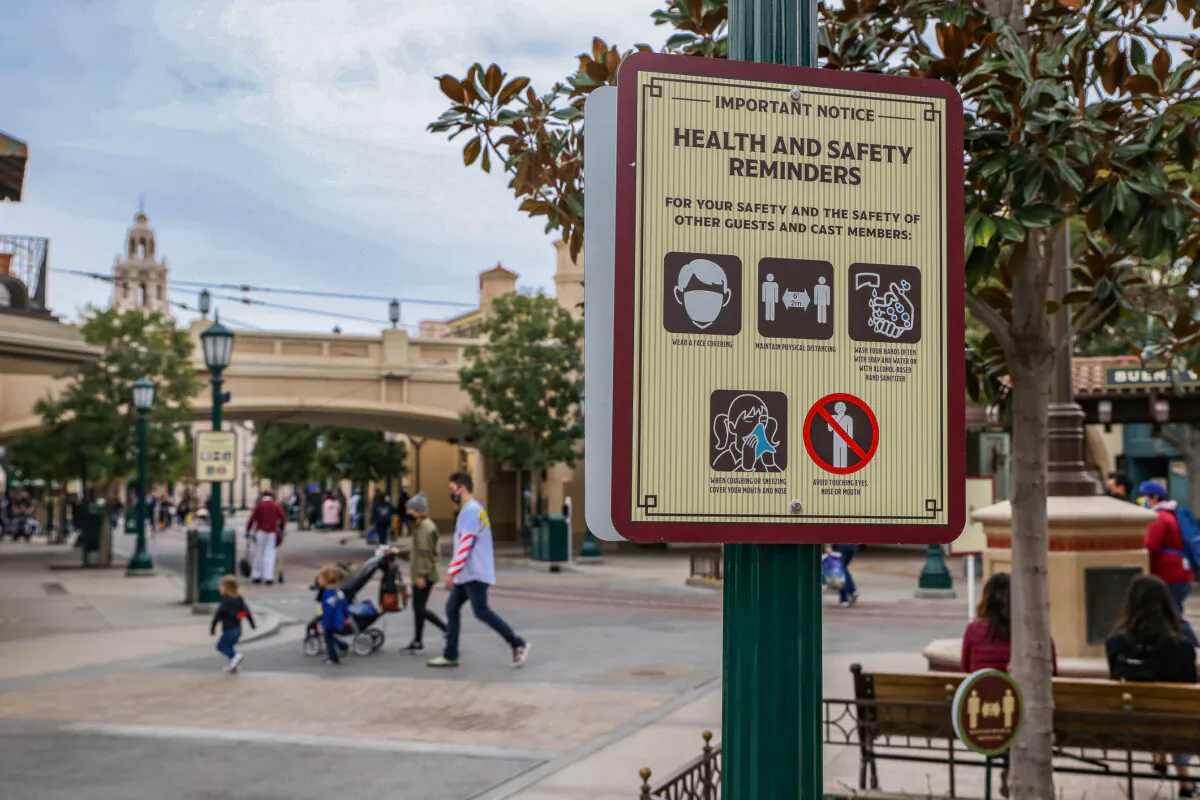 A family walks by a COVID-19 safety sign at Disneyland California Adventure themepark in Anaheim, Calif., on Feb. 1, 2021. (John Fredricks/The Epoch Times)