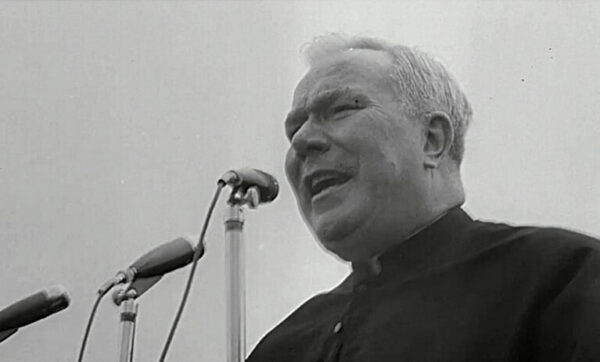 priest in front of microphone in "Pray"