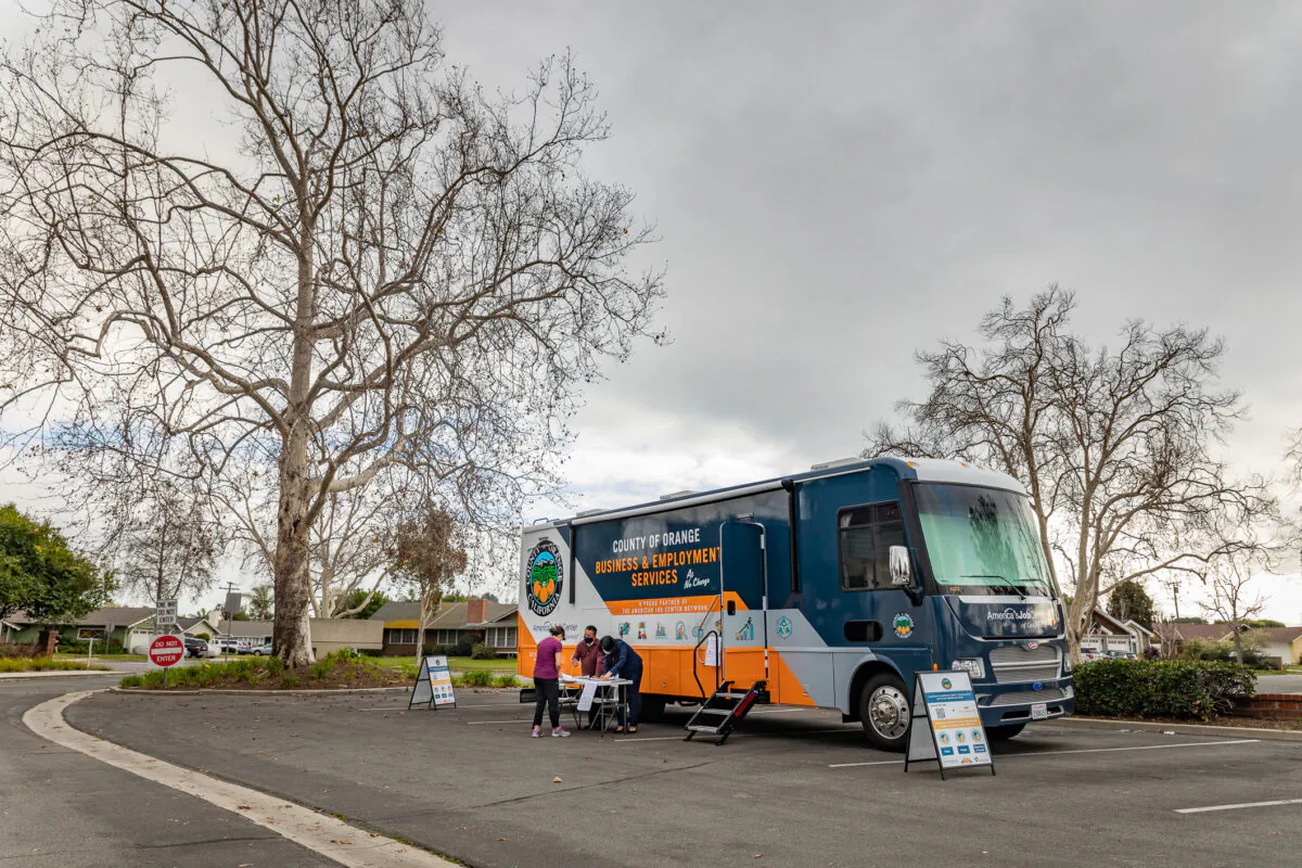 Caseworkers talk with a woman in search of work next to a  County of Orange business and employment services bus parked for the day for scheduled appointments at the Rossmoor Library in Rossmoor, Calif., on Feb. 9, 2021. (John Fredricks/The Epoch Times)