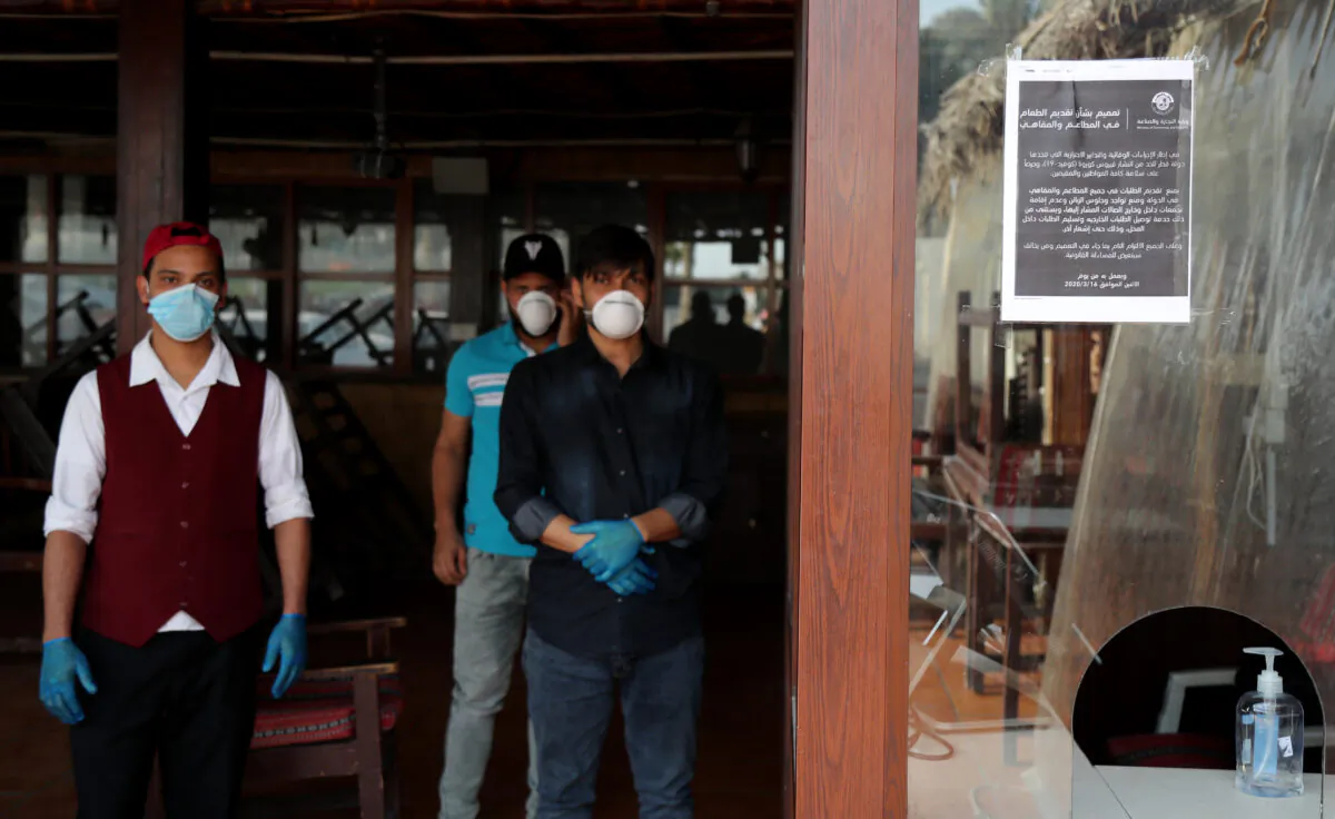Mask-clad workers stand inside a closed-down cafe in Qatar's capital Doha on March 16, 2020. (Qatar Out/AFP via Getty Images)