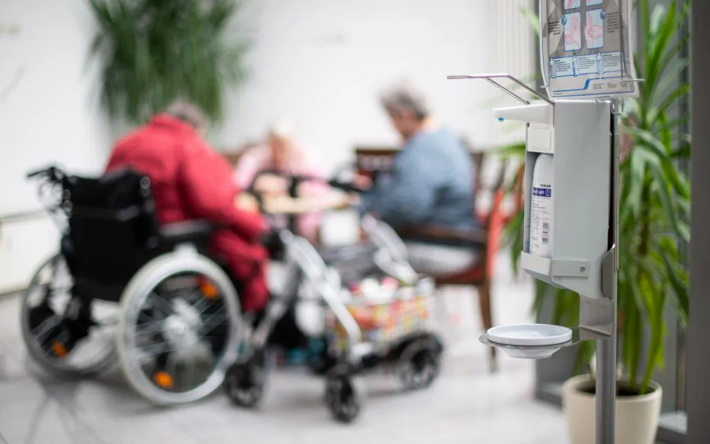 Residents sit near a hand sanitizer dispenser at a long-term care home. (Photo by Jonas Güttler/Picture Alliance via Getty Images)