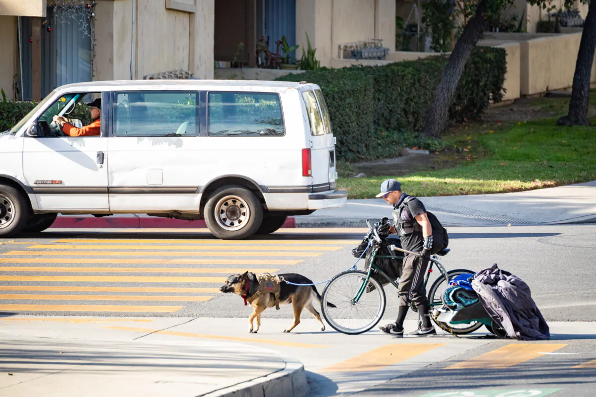 A homeless man walks with his bike, dog, and possessions in Santa Ana, Calif., on Dec. 17, 2020. (John Fredricks/The Epoch Times)