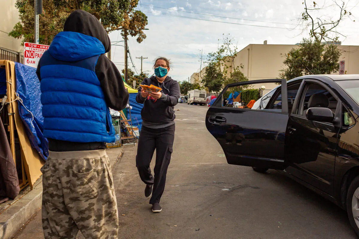 A woman hands items to a homeless man in the Venice neighborhood of Los Angeles on Jan. 27, 2021. (John Fredricks/The Epoch Times)