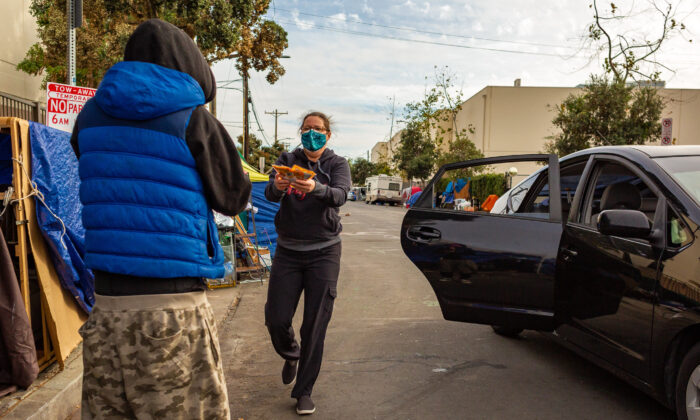 A woman hands items to a homeless man in the Venice neighborhood of Los Angeles on Jan. 27, 2021. (John Fredricks/The Epoch Times)