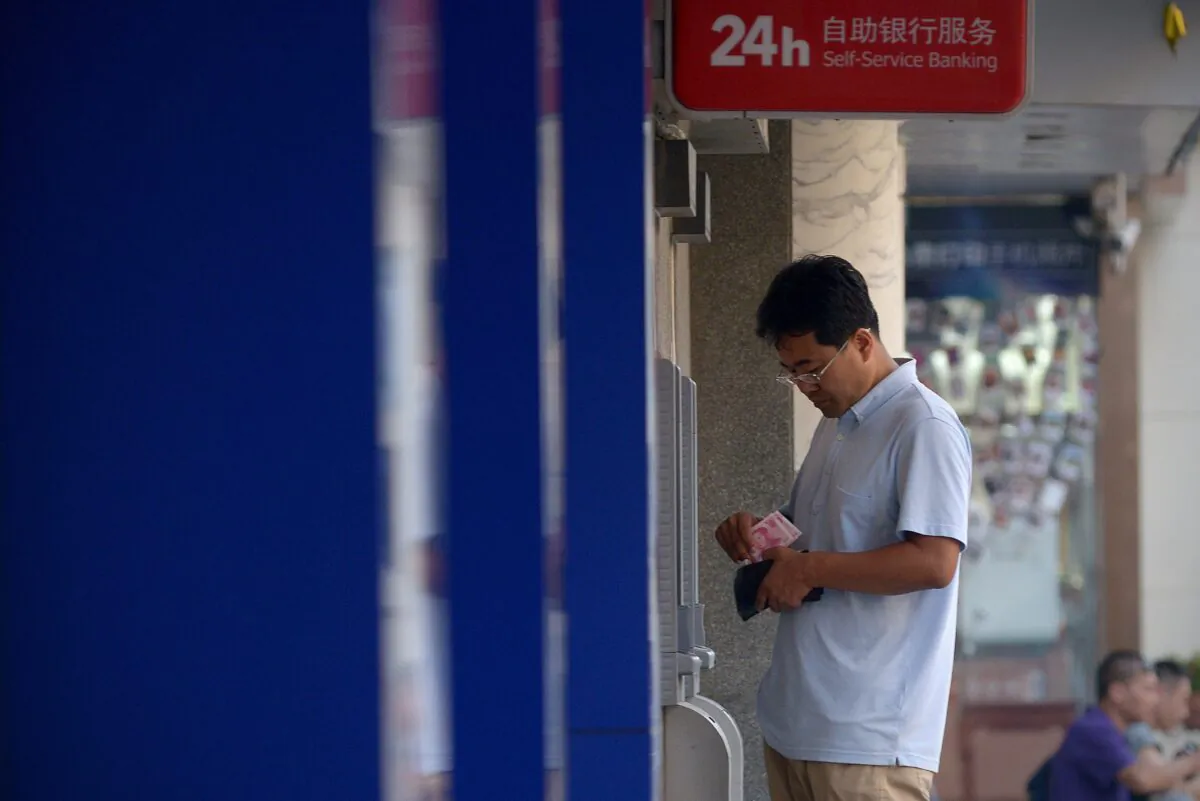 A man counts money in front of an automatic teller machine at the entrance of a bank in Beijing on Aug. 13, 2015. (WANG ZHAO/AFP via Getty Images)