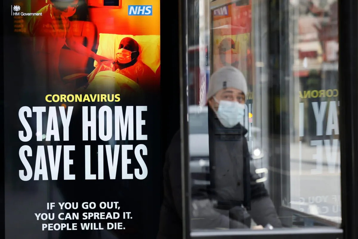 A commuter wears a face mask as he sits in a bus shelter with NHS signage promoting "Stay Home, Save Lives" in the Chinatown section of London on Jan. 8, 2021. (Tolga Akmen /AFP via Getty Images)
