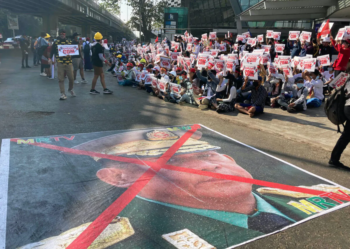 A large image that has an X mark on the face of Commander in chief Senior Gen. Min Aung Hlaing, also chairman of the State Administrative Council, lies on a road as anti-coup protesters gather outside the Hledan Centre in Yangon, Burma, on Feb. 14, 2021. (AP Photo)