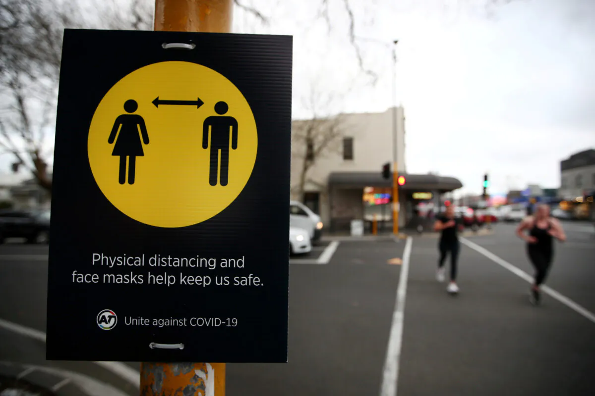 People jog past a social distancing sign on the first day of New Zealand's new coronavirus disease (COVID-19) safety measure that mandates wearing of a mask on public transport, in Auckland, New Zealand, on Aug. 31, 2020. (Fiona Goodall/ Reuters)