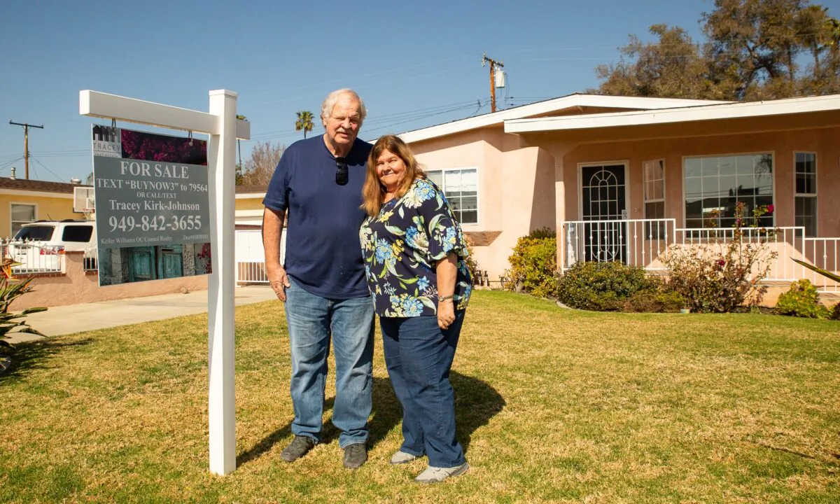 John Peterson and his wife stand next to a for-sale sign on their lawn in Garden Grove, Calif., on Feb. 7, 2021. (John Fredricks/The Epoch Times)