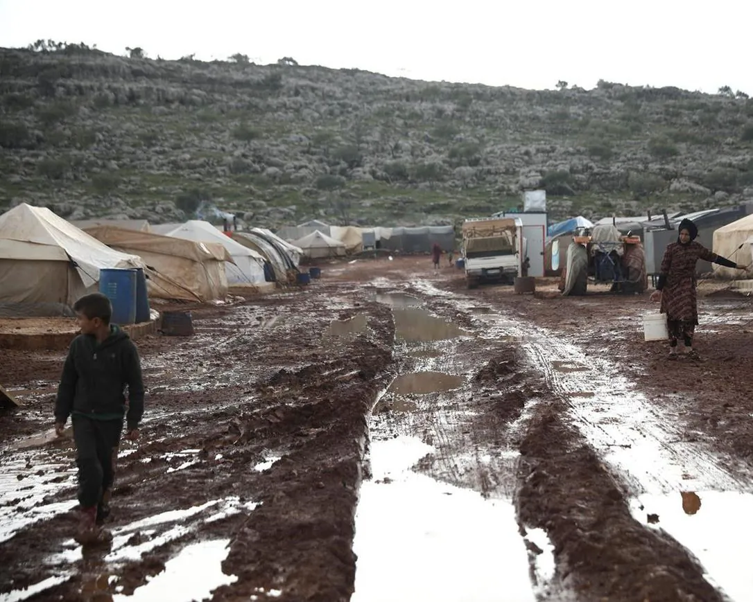 Syrian refugees walk through a camp for the displaced muddied by recent rains near the village of Kafr Aruq, in Idlib province, Syria, on Jan. 28, 2021. A United Nations rights' advocate and Human Rights Watch Canada say the Trudeau government isn't living up to its new international campaign against arbitrary detention because it is abandoning 25 Canadian children trapped in northern Syria.  (Ghaith Alsayed/AP/The Canadian Press)