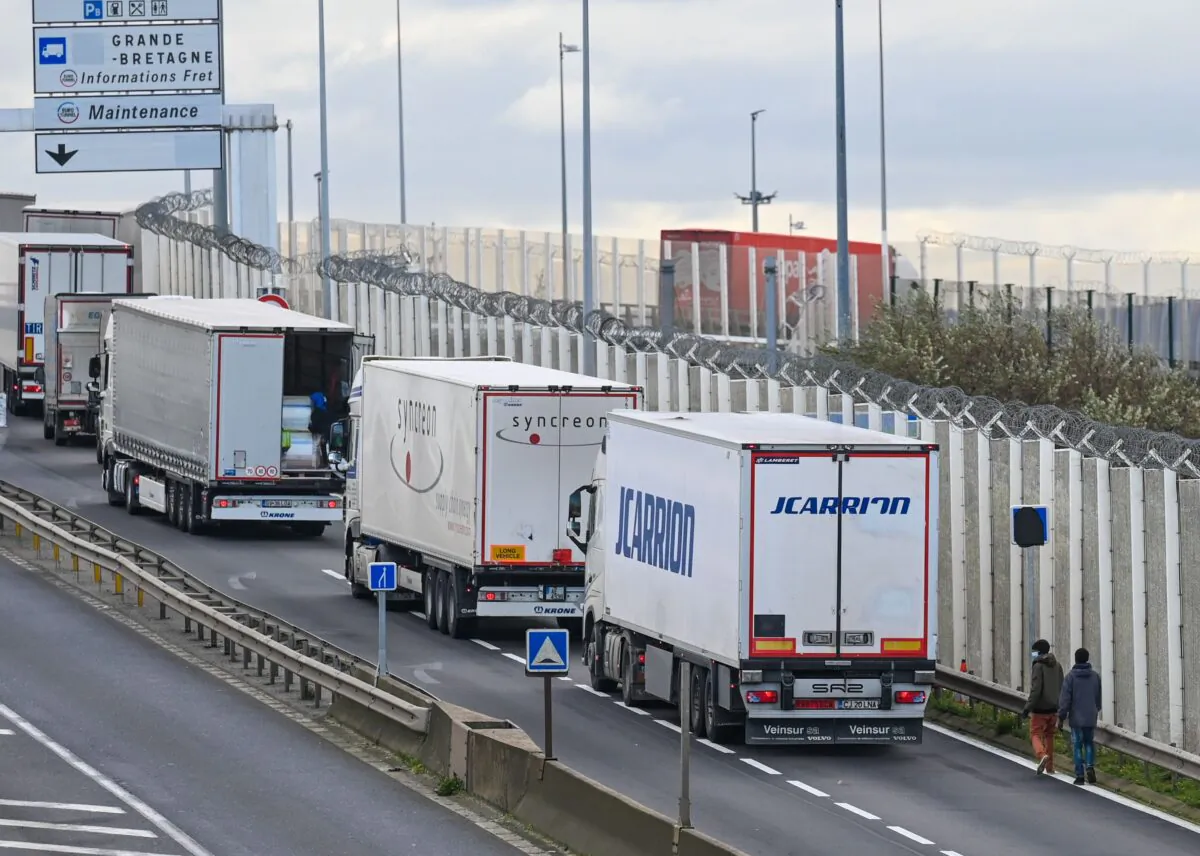 Migrants walk to climb into the back of lorries bound for Britain while traffic is stopped upon waiting to board shuttles at the entrance to the Channel Tunnel site in Calais, northern France, on Nov. 19, 2020. (Denis Charlet/AFP via Getty Images)