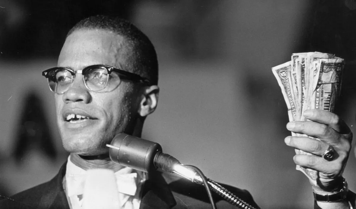 Headshot of American political activist Malcolm X (1925 - 1965) holding a fist full of U.S. currency during a speech at Urline Arena, Washington, in August 1963. (Richard Saunders/Hulton Archive/Getty Images)