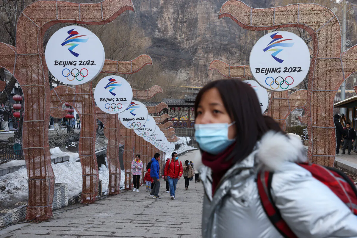 People wear protective masks as they walk in front of logos for the 2022 Beijing Winter Olympics at Yanqing Ice Festival in Beijing, on Feb. 26, 2021. (Lintao Zhang/Getty Images)