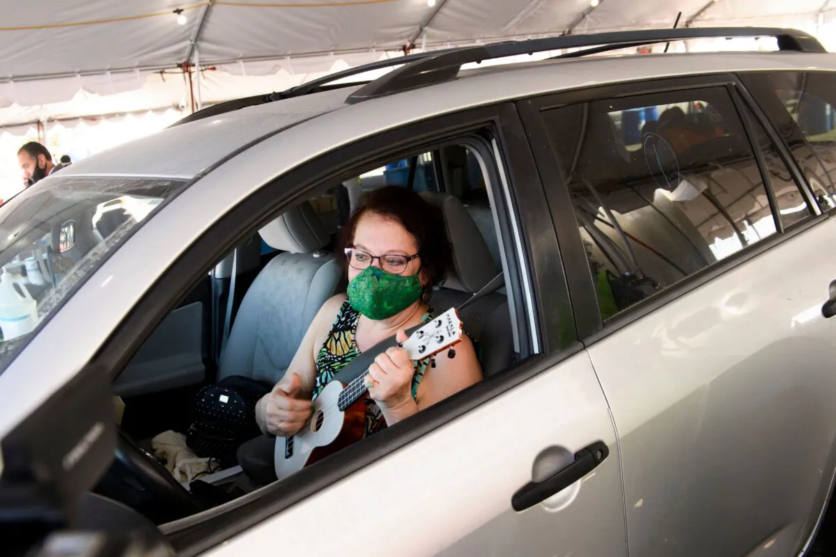 A Los Angeles Unified School District teacher plays the ukulele as she waits to receive a COVID-19 vaccination at a mass vaccination site in a parking lot at Hollywood Park in Inglewood, Calif., on March 1, 2021. (Patrick T. Fallon/AFP via Getty Images)