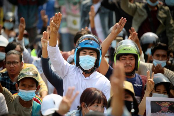 Anti-coup protesters flash a three-fingered sign of resistance