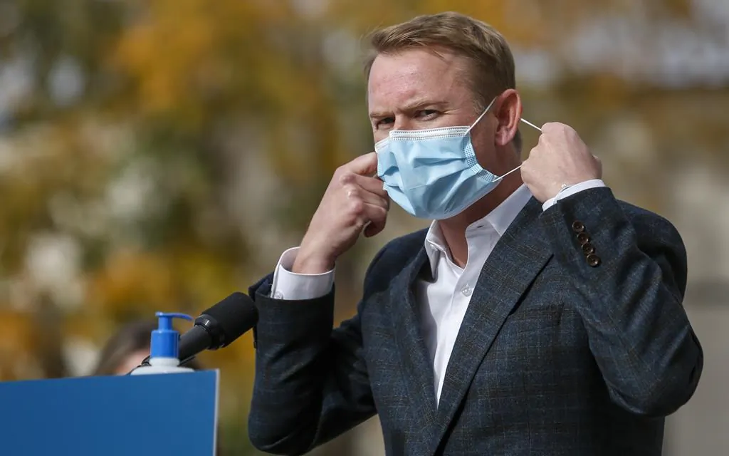 Minister of Health Tyler Shandro, removes his made-in-Calgary mask while announcing a new agreement between Alberta Health Services and a local manufacturer to produce medical equipment, in Calgary, Alta., Oct. 7, 2020. (Jeff McIntosh/The Canadian Press)
