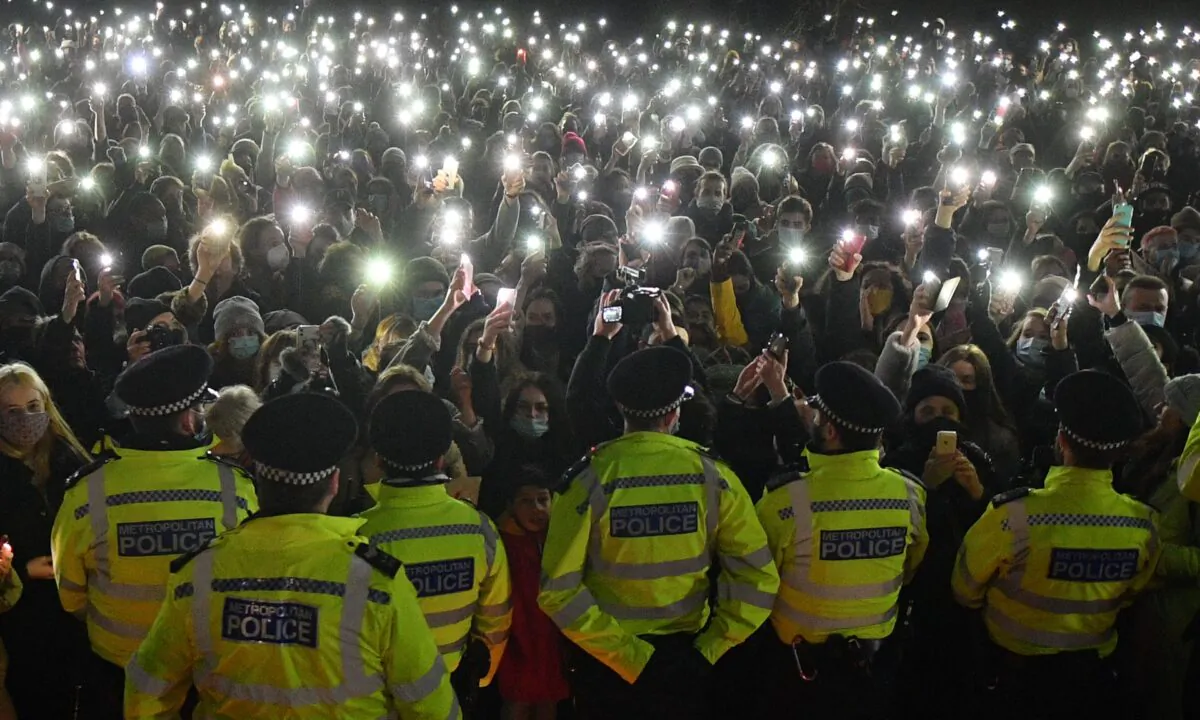 Police officers form a cordon as a crowd turn on their phone torches at a band-stand where a planned vigil in honour of murder victim Sarah Everard was cancelled due to CCP virus restrictions, on Clapham Common, south London on March 13, 2021. (Justin Tallis/AFP via Getty Images)
