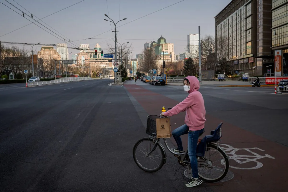 A woman wearing a mask sits on her bicycle at a red light on a nearly empty street in Beijing on March 22, 2020. (Nicolas Asfouri/AFP via Getty Images)