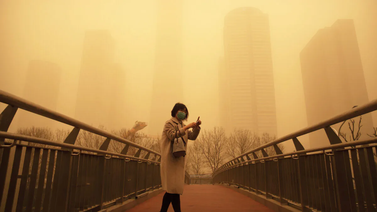 A woman walks along a pedestrian bridge amid a sandstorm during the morning rush hour in the central business district in Beijing on March 15, 2021. (Mark Schiefelbein/AP)