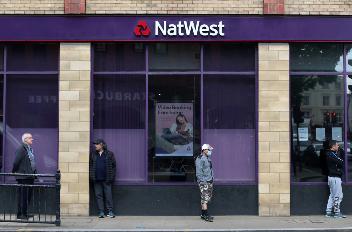 People maintain social distance while they queue outside a NatWest bank in Wimbledon, London, on May 1, 2020. (Hannah McKay/Reuters)