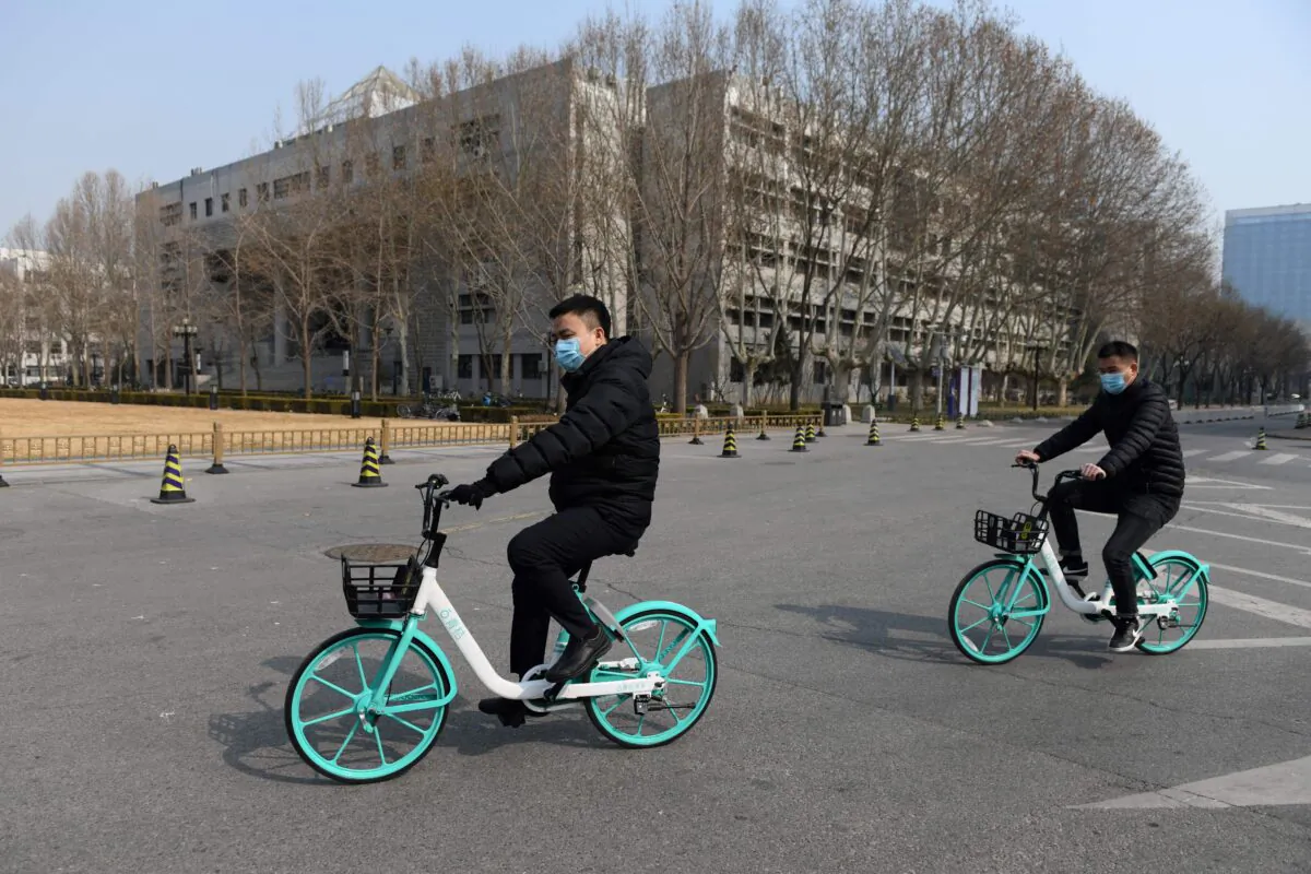 Two men ride bikes in the empty grounds of Tsinghua University in Beijing on Feb. 28, 2020. (Greg Baker/AFP via Getty Images)