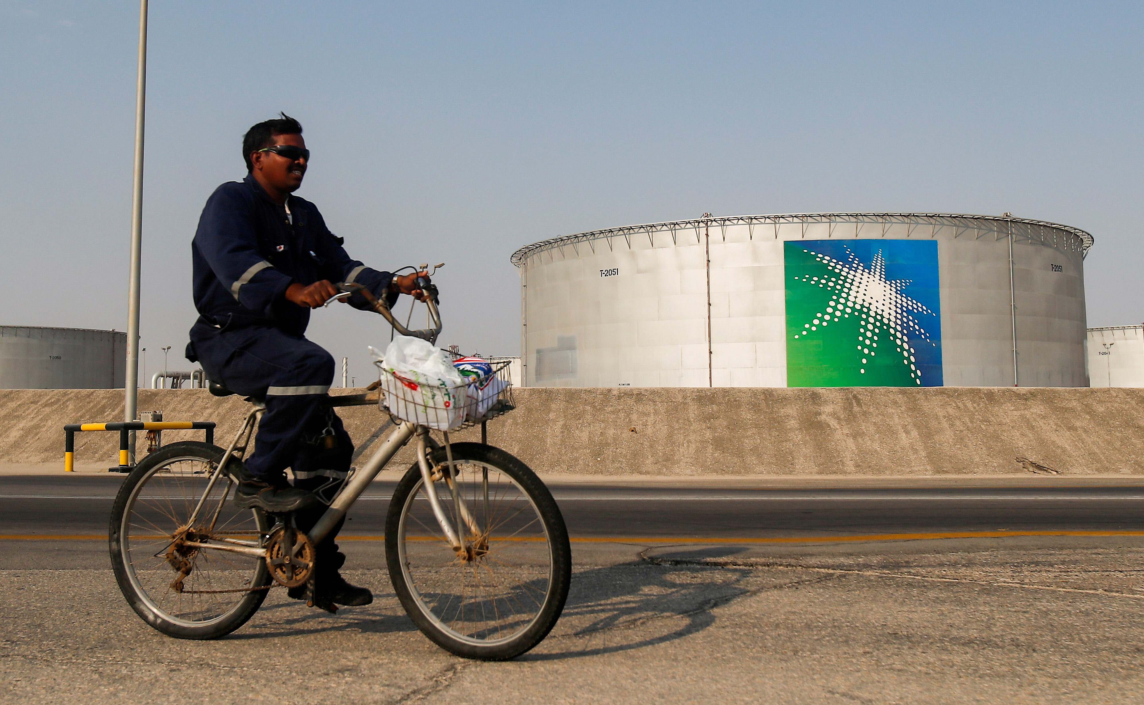 FILE PHOTO: An employee rides a bicycle next to oil tanks at Saudi Aramco oil facility in Abqaiq