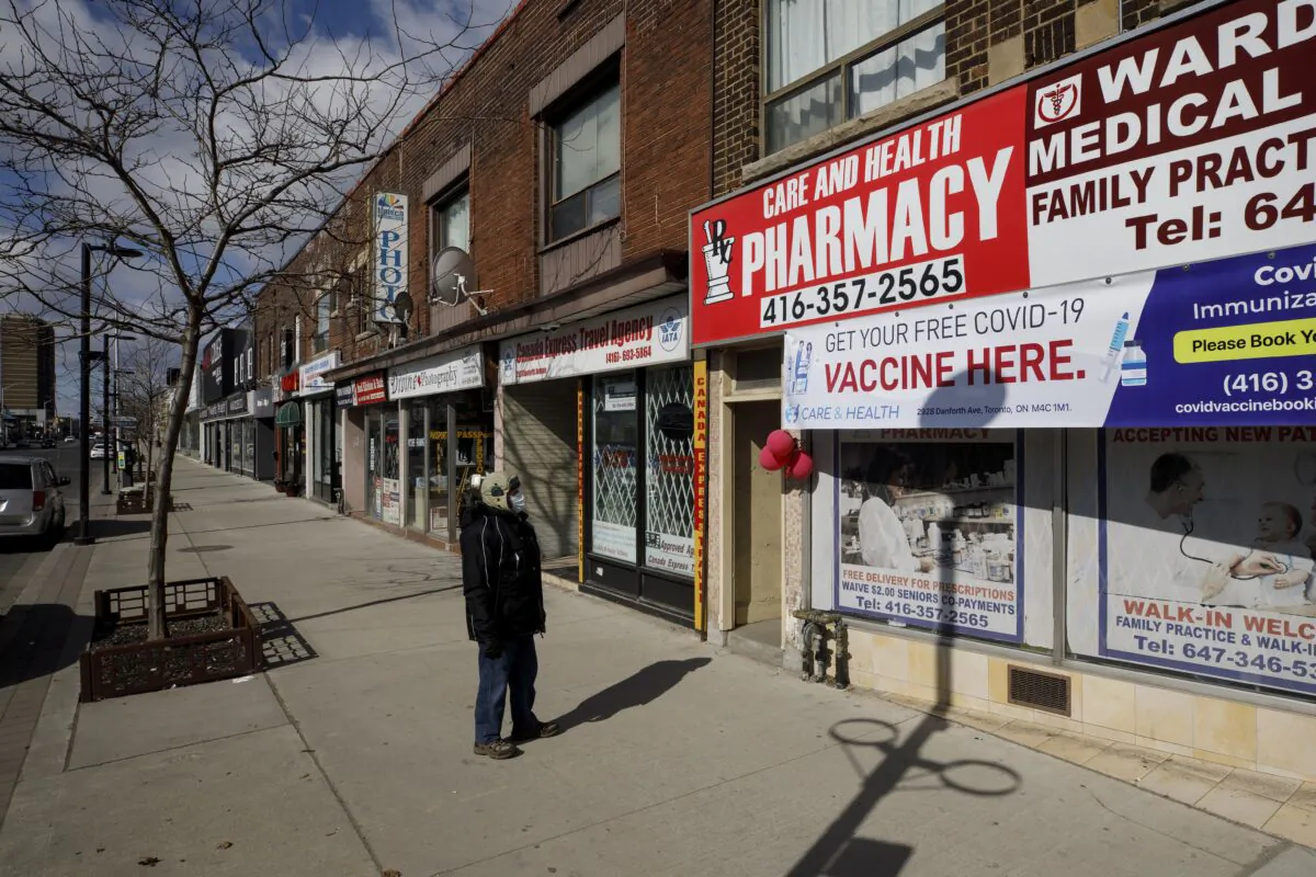 A pedestrian looks at a sign offering free COVID-19 vaccines at a pharmacy on an empty street in Toronto on March 14, 2021. (The Canadian Press/Cole Burston)