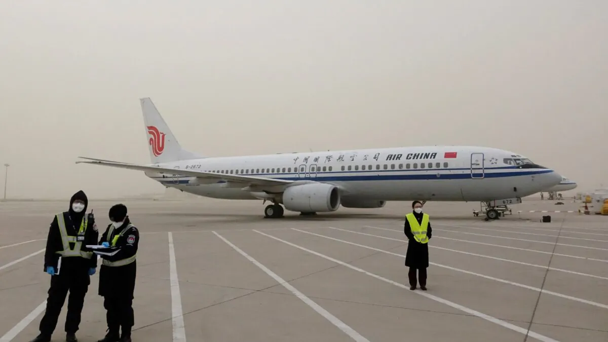 Staff members stand near a Boeing 737-800 airplane of Air China on the tarmac of Beijing Capital International Airport, which is shrouded in dust as the city is hit by a sandstorm, in Beijing, China, on March 28, 2021. (Carlos Garcia Rawlins/Reuters)