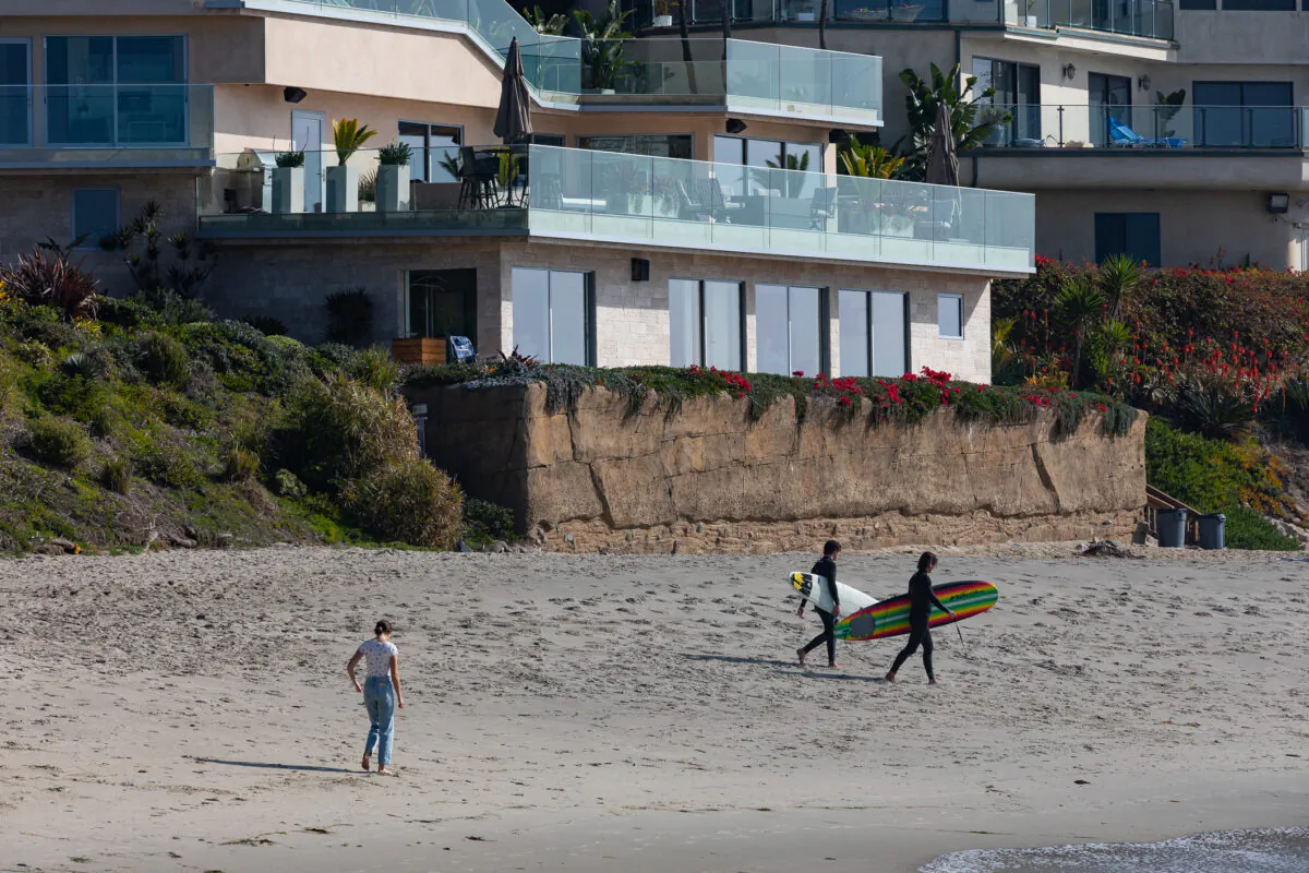 Surfers walk past a seawall built in front of a home at Victoria Beach, in the city of Laguna Beach, Calif., on Jan. 8, 2021. (John Fredricks/The Epoch Times)