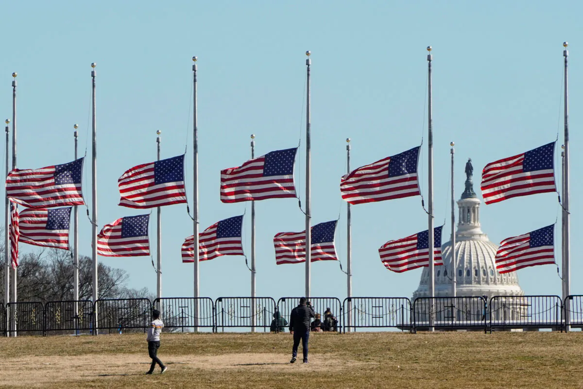 People walk past flags flying at half staff at the Washington Monument in memory of 500,000 deaths due to COVID-19 in Washington, on Feb. 24, 2021. (Joshua Roberts/Reuters)