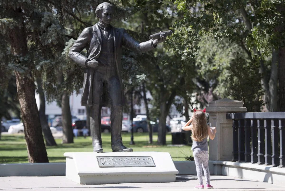 A little girl stops to look at a statue of John A. Macdonald in Victoria Park in Regina, Canada, on Aug. 22, 2018. (Jonathan Hayward/The Canadian Press)