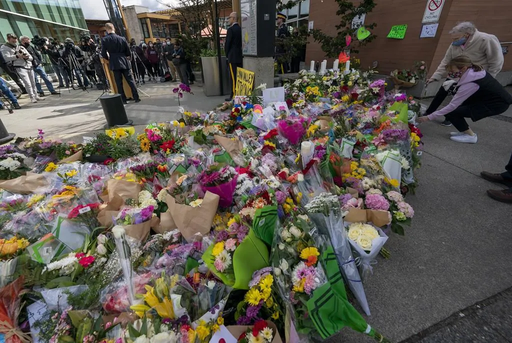 A lady places flowers at a makeshift memorial as the RCMP give a news conference outside of the Lynn Valley Library in Lynn Valley in North Vancouver, B.C., on March 29, 2021. (The Canadian Press/Jonathan Hayward)