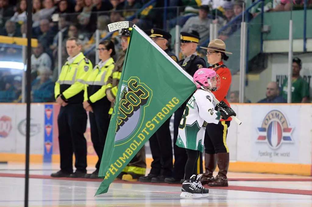 A girl skates with a Humboldt Broncos flag as she skates by first responders during a tribute to the team after their SJHL game against the Nipawin Hawks in Humboldt, Sask., on Sept. 12, 2018. The City of Humboldt has announced an ambitious plan to permanently commemorate the deadly Broncos bus crash. (Jonathan Hayward / The Canadian Press)
