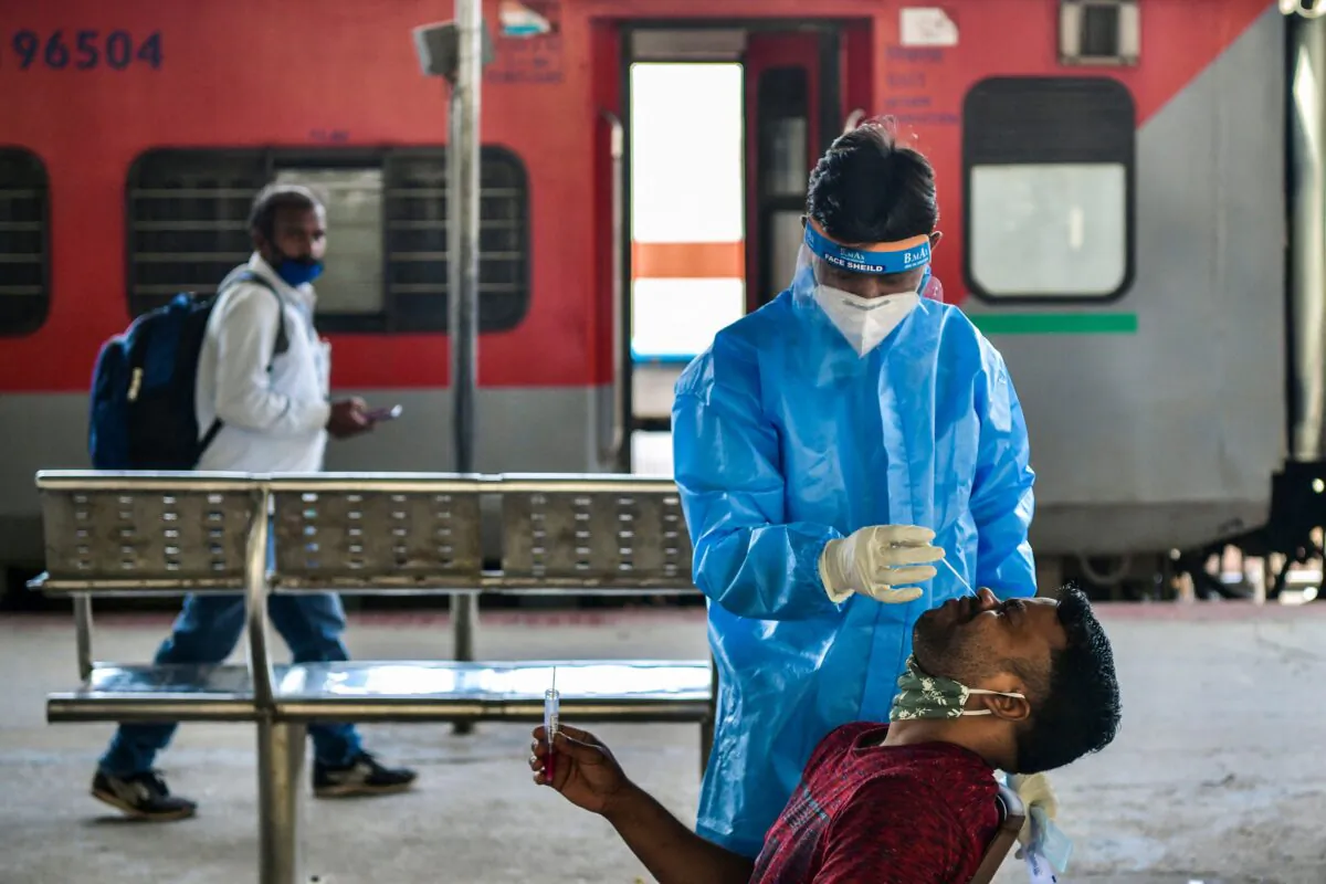 A health worker collects a sample from a passenger for a Reverse Transcription Polymerase Chain Reaction (RT-PCR) test at the Yesvantpur railway station in Bangalore on April 5, 2021. (Manjunath Kiran /AFP via Getty Images)