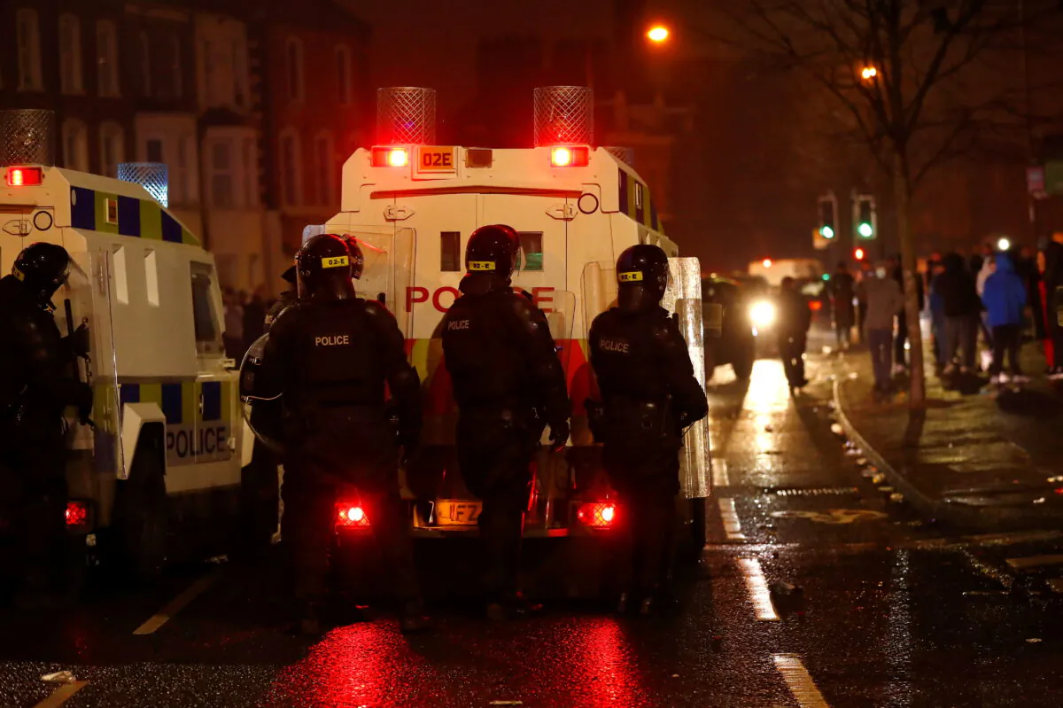 Police officers behind shields stand behind a police vehicle on Springfield Road as protests continue in Belfast, Northern Ireland, on April 7, 2021. (Jason Cairnduff/Reuters)
