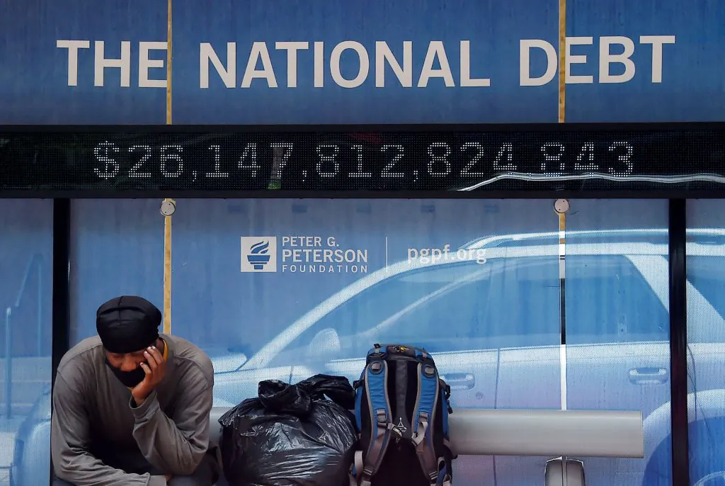 A man waits at a bus stop that displays the national debt of the United States in Washington, on June 19, 2020. (Olivier Douliery/AFP via Getty Images)
