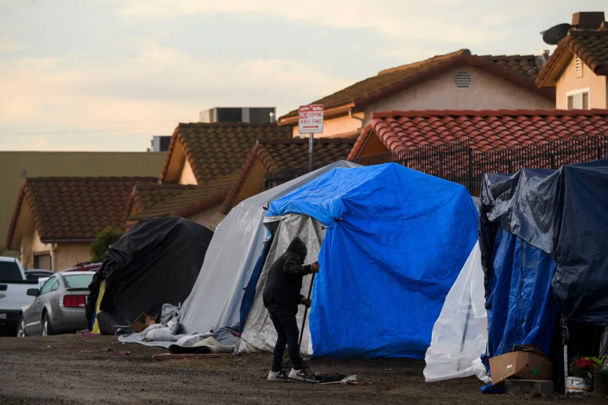 People experiencing homelessness clean the area around their tent shelters before a Los Angeles City Bureau of Sanitation cleanup sweep of homeless encampments in the area during the COVID-19 pandemic, in the Harbor City neighborhood of Los Angeles, on Jan. 28, 2021. (Patrick T. Fallon/AFP via Getty Images)