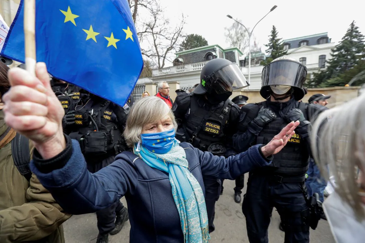 A woman holds an EU flag next to police officers during a protest over the Russian intelligence services alleged involvement in an ammunition depot explosion in Vrbetice area in 2014, outside the Russian Embassy in Prague, Czech Republic, on April 18, 2021. (David W Cerny/Reuters)