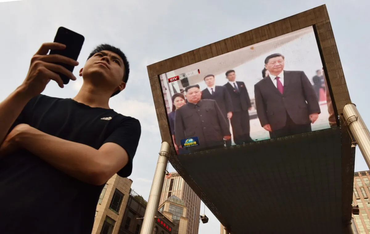 A man waits for a taxi as news footage of Chinese leader Xi Jinping (R) being greeted in Pyongyang by North Korean leader Kim Jong Un is shown on a large screen behind him outside a shopping mall in Beijing, China, on June 20, 2019. (Greg Baker/AFP via Getty Images)