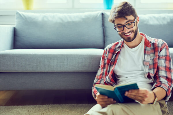 Portrait,Of,Joyful,Young,Man,Reading,Book,While,Sitting,On
