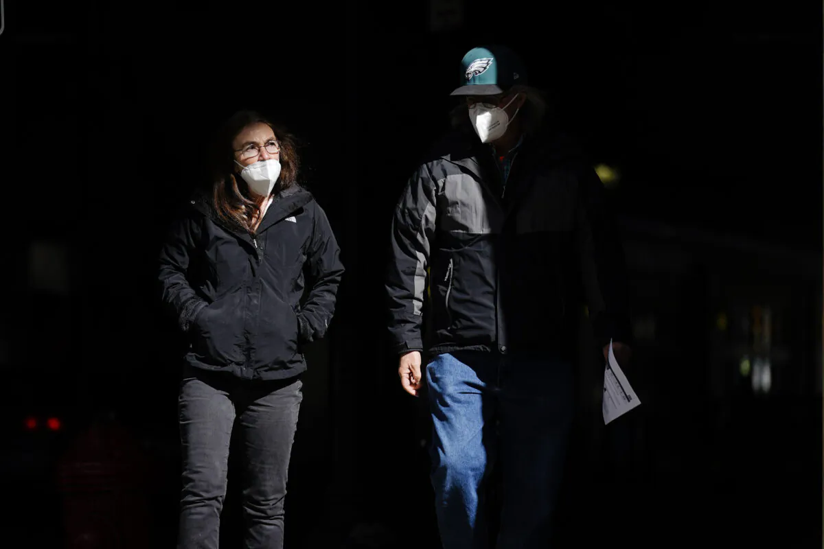 People wearing masks walk through a shaft of light on a street in Philadelphia, Pa., on March 3, 2021. (Matt Rourke/AP Photo)