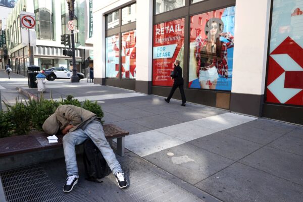 A homeless person sleeps on a bench