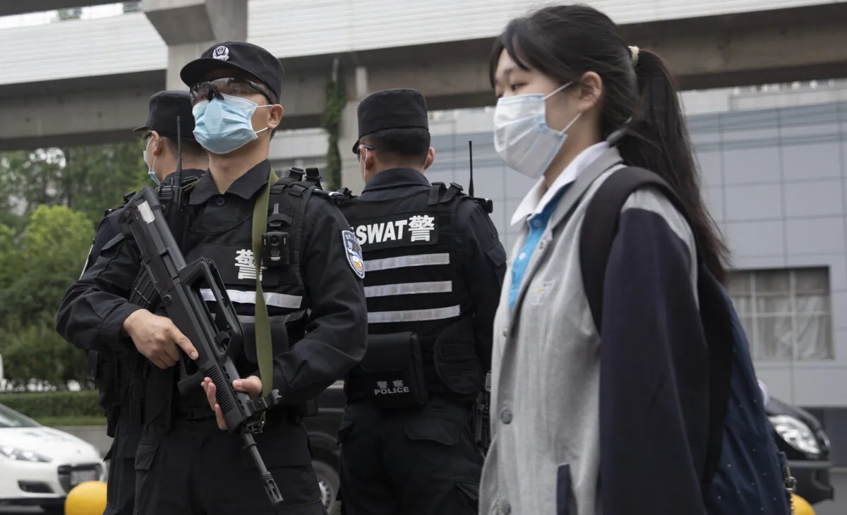 Police officers (L) stand guard at an entrance of a high school as a senior student walks past in Wuhan City of Hubei province, China on May 6, 2020. (STR/AFP via Getty Images)