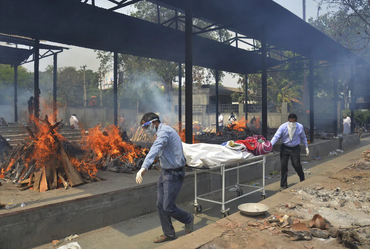 Relatives carry the body of a person who died of COVID-19 as multiple pyres of other victims burn at a crematorium in New Delhi, India, on May 1, 2021. (Amit Sharma/AP Photo)