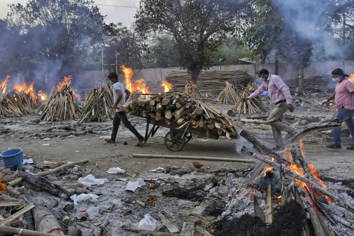 A worker carries wood on a hand cart as multiple funeral pyres of COVID-19 victims burn at a crematorium on the outskirts of New Delhi, India, on May 1, 2021. (Ishant Chauhan/AP Photo)