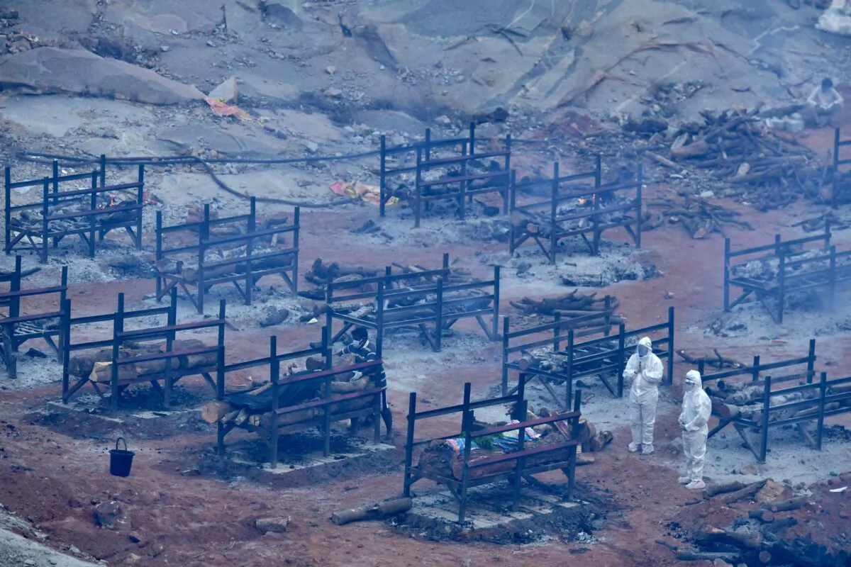 Family members wearing protective gear offer prayers next to the pyre of a victim who died of COVID-19 at an open air crematorium set up for the coronavirus victims inside a defunct granite quarry on the outskirts of Bangalore, India, on May 1, 2021. (Manjunath Kiran/AFP via Getty Images)